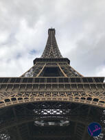 Looking up at the Eiffel Tower in Paris, showing the intricate architectural iron lattice against a cloudy sky.