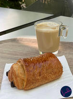 A flaky golden pain au chocolat served with a glass latte on a Paris café table in the morning light.