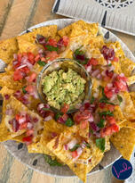 A plate of nachos topped with melted cheese, diced tomato, onions, and cilantro, served with fresh guacamole in Madrid.