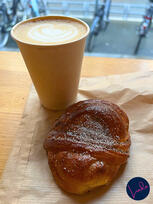 A spiced Swedish-style cardamom bun sprinkled with sugar, paired with a latte in a paper cup at a cozy café.