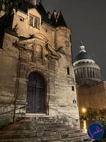 Illuminated stone steps leading to an old Paris building at night, with the dome of the Panthéon rising in the background.