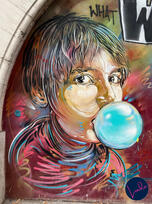Vibrant Paris street art of a young boy blowing a large bubble gum bubble, painted in bold swirling colors.