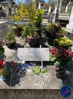 The grave of French singer Serge Gainsbourg in Montparnasse Cemetery, decorated with flowers, plants, and tributes.
